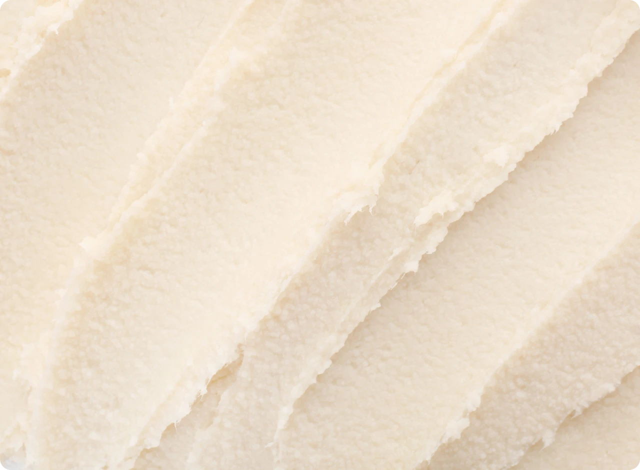 Dünne Schichten von sheabutter in einer cremigen, hellen Textur, die gleichmäßig auf einer Oberfläche verteilt sind.