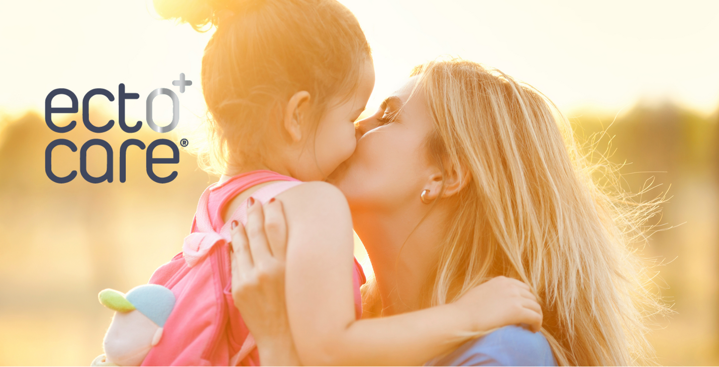 Eine Frau küsst ein junges Mädchen in sanftem Sonnenlicht liebevoll auf die Wange. Das Mädchen hält ein Plüschtier in der Hand, und beide wirken glücklich. Das ecto care Logo ist auf der linken Seite des Bildes zu sehen.