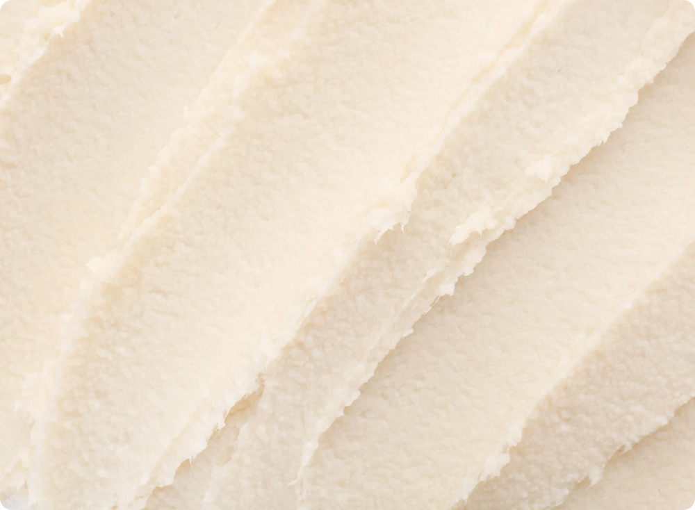 Dünne Schichten von sheabutter in einer cremigen, hellen Textur, die gleichmäßig auf einer Oberfläche verteilt sind.